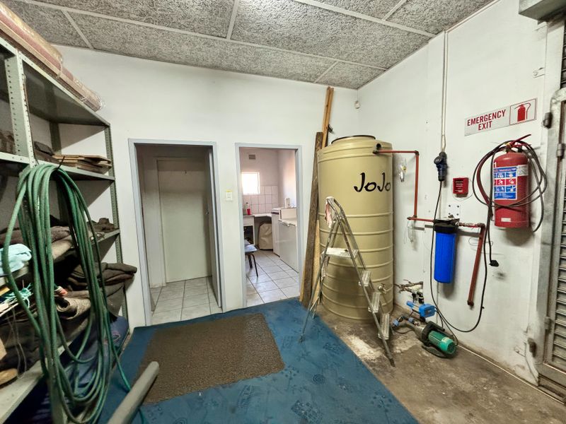 Utility storage area featuring a water tank, pump system, fire safety equipment, and metal shelving, providing functional space for building maintenance and storage.