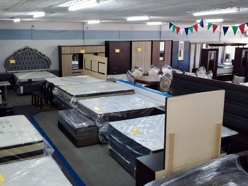 A large open-plan retail showroom space featuring suspended ceilings, fluorescent lighting, and carpeted flooring, currently utilized for furniture display.