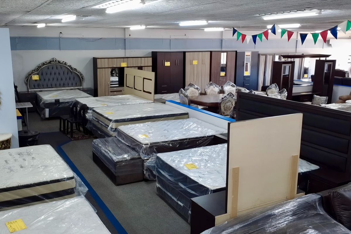 A large open-plan retail showroom space featuring suspended ceilings, fluorescent lighting, and carpeted flooring, currently utilized for furniture display.