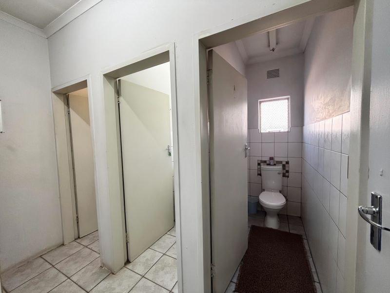 A functional hallway area providing access to multiple rooms, featuring tiled flooring and a separate toilet facility with ceramic wall tiling.