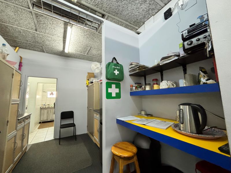 A functional utility or staff break area featuring built-in shelving, a fixed counter, and a suspended ceiling, providing access to an adjacent room.