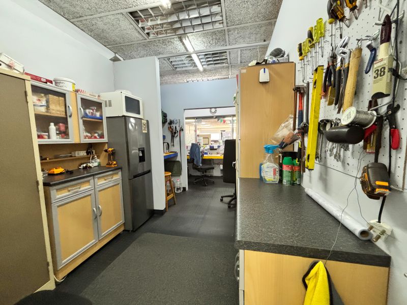 A functional utility or staff break area featuring laminate cabinetry, countertop workspace, and integrated pegboard storage, with a drop ceiling and fluorescent lighting.