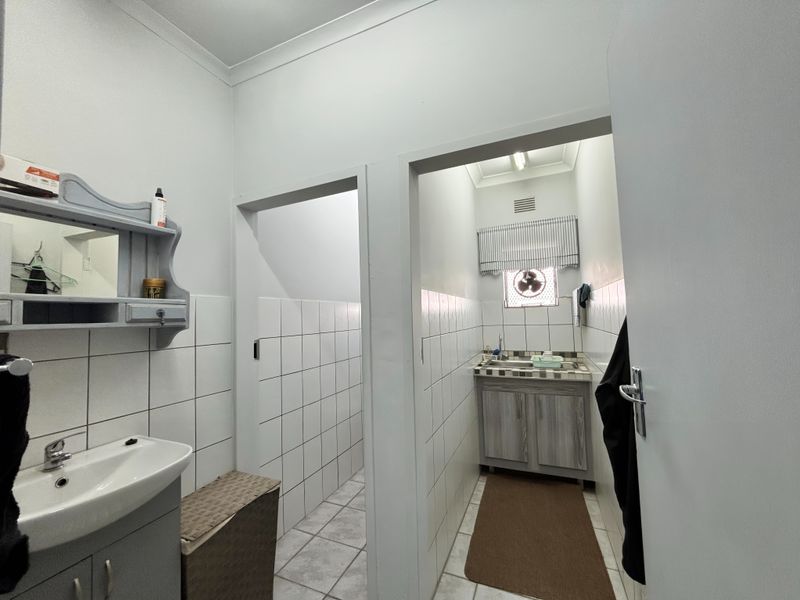 A functional bathroom area featuring tiled walls, a vanity cabinet with a sink, and a separate wash-up or utility space with an extractor fan.