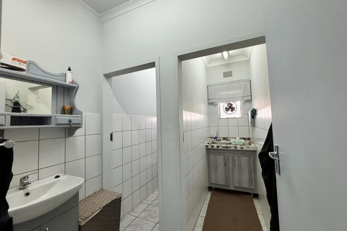 A functional bathroom area featuring tiled walls, a vanity cabinet with a sink, and a separate wash-up or utility space with an extractor fan.