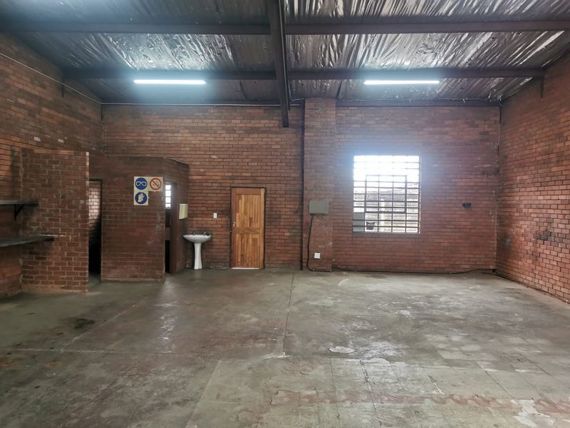 Spacious industrial utility area featuring exposed brick walls, concrete flooring, and high ceilings with exposed steel beams and functional lighting.