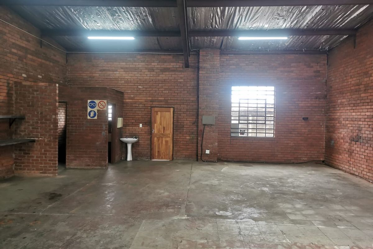 Spacious industrial utility area featuring exposed brick walls, concrete flooring, and high ceilings with exposed steel beams and functional lighting.