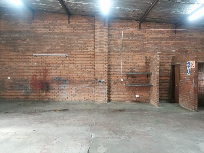 Spacious industrial utility area featuring exposed brick walls, concrete flooring, and high ceilings with industrial lighting, suitable for workshop or storage use.