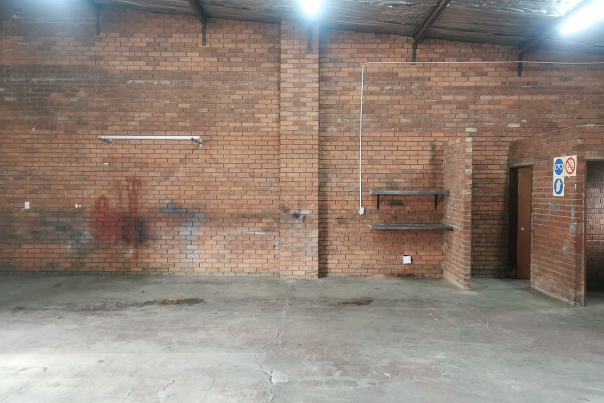 Spacious industrial utility area featuring exposed brick walls, concrete flooring, and high ceilings with industrial lighting, suitable for workshop or storage use.