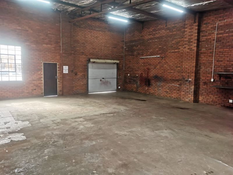 Spacious industrial utility area featuring exposed brick walls, concrete flooring, and a roller shutter door, suitable for workshop or storage use.
