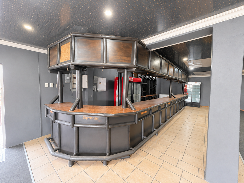 A spacious commercial bar area featuring a large built-in counter, tiled flooring, and recessed ceiling lighting, suitable for hospitality or retail use.