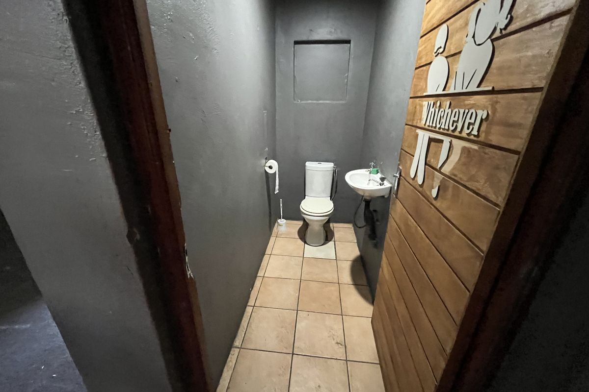 A compact restroom featuring a toilet, wall-mounted basin, and tiled flooring, finished with dark grey walls and a wooden door.