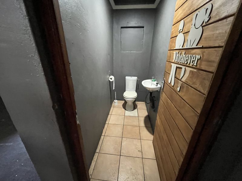A compact restroom featuring a toilet, wall-mounted basin, and tiled flooring, finished with dark grey walls and a wooden door.