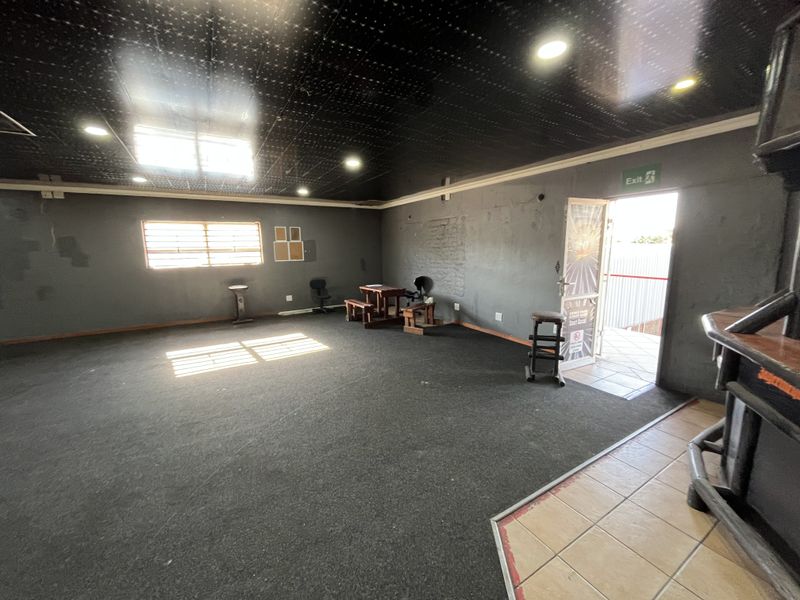 Spacious open-plan retail area featuring dark carpeted flooring, a black ceiling with recessed lighting, and direct access to an exterior entrance.