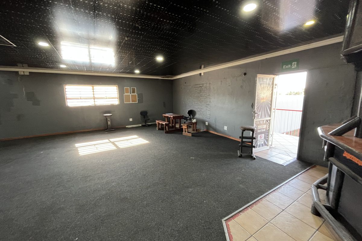 Spacious open-plan retail area featuring dark carpeted flooring, a black ceiling with recessed lighting, and direct access to an exterior entrance.