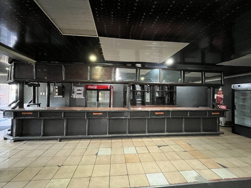A spacious bar area featuring a long built-in counter, tiled flooring, and integrated refrigeration units, offering significant potential for renovation and modernization.