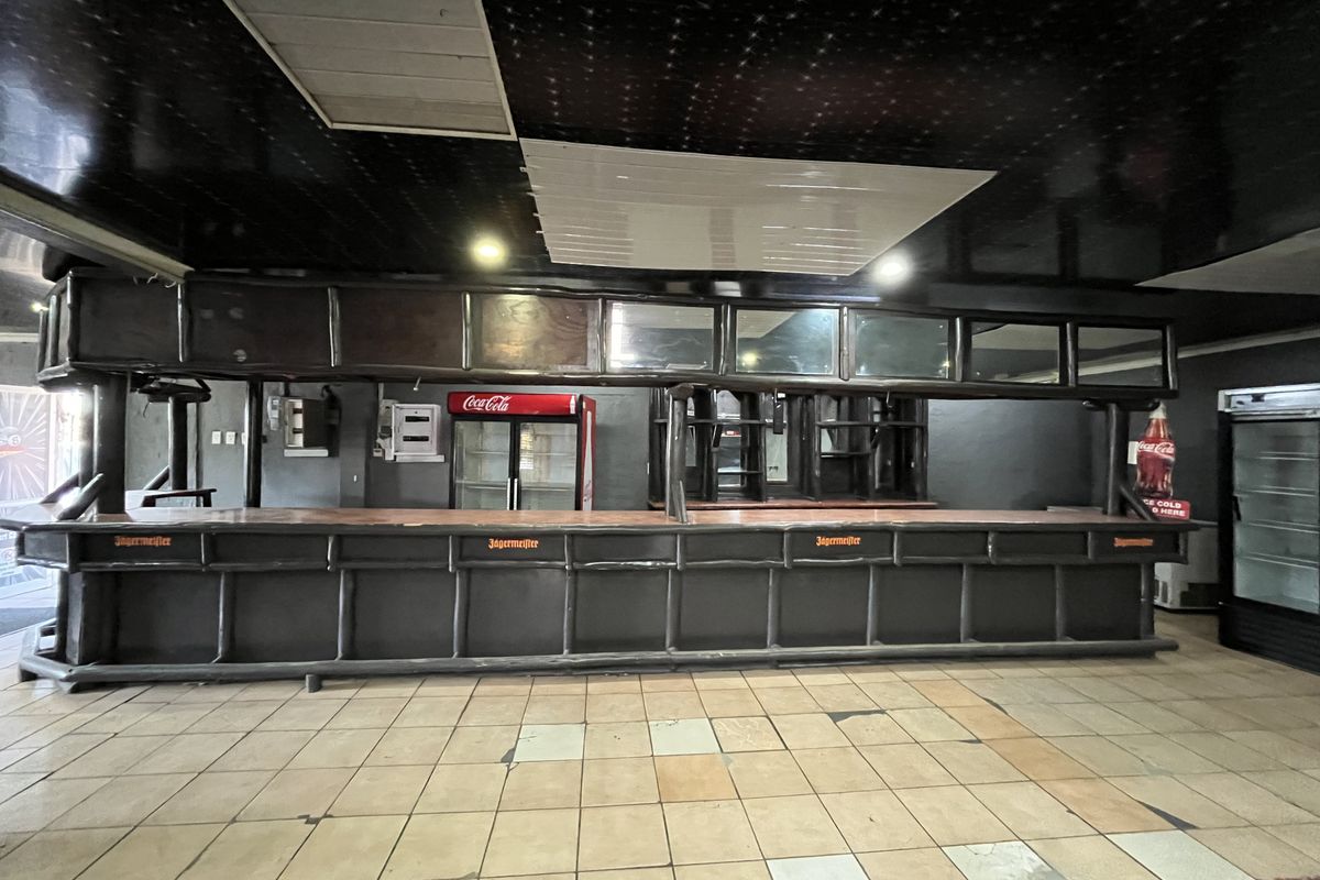 A spacious bar area featuring a long built-in counter, tiled flooring, and integrated refrigeration units, offering significant potential for renovation and modernization.