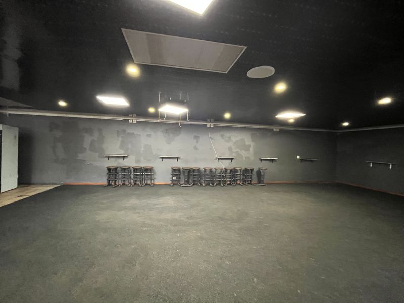 Spacious open-plan retail area featuring dark finishes, recessed lighting, and wall-mounted shelving, currently in need of cosmetic refurbishment.