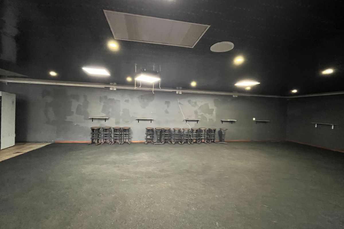 Spacious open-plan retail area featuring dark finishes, recessed lighting, and wall-mounted shelving, currently in need of cosmetic refurbishment.