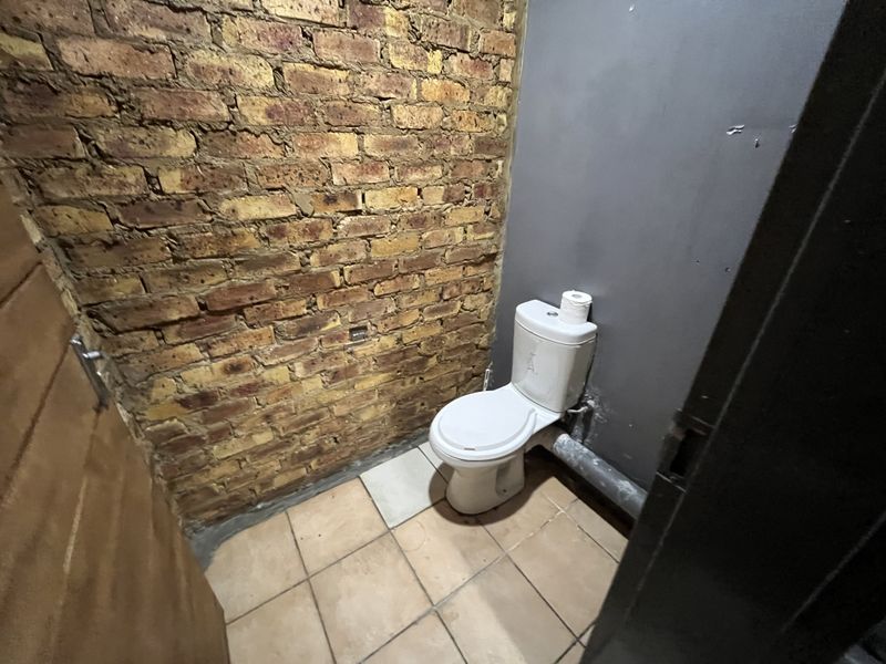 A small, unfinished bathroom featuring an exposed brick wall, tiled flooring, and a standard toilet with visible plumbing.