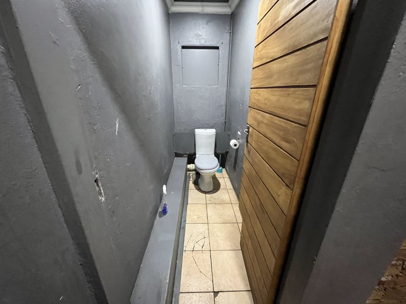 A small, utilitarian bathroom featuring a toilet, tiled flooring, and a wooden door, currently requiring maintenance and cosmetic updates.