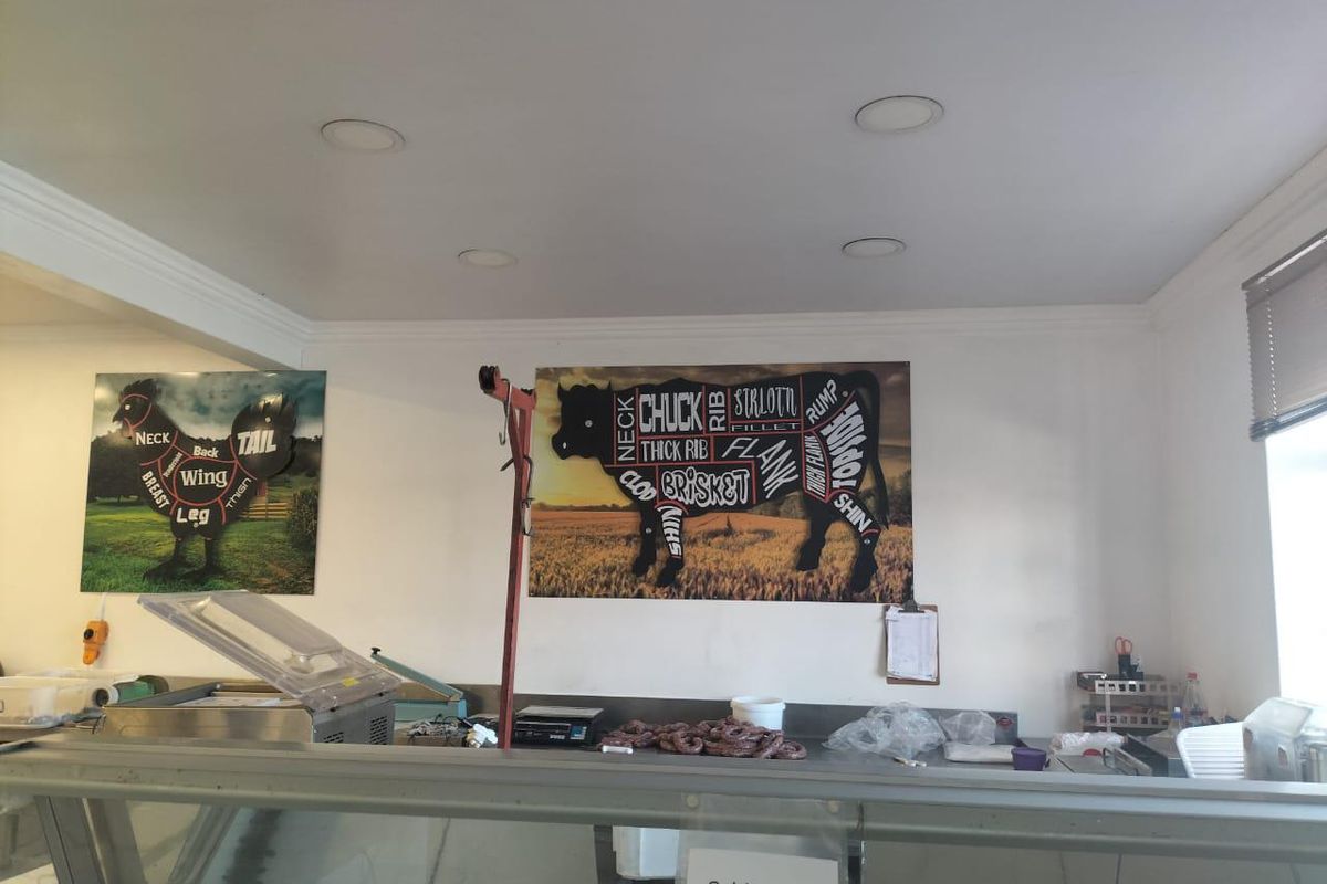 A functional industrial butchery prep area featuring a service counter, recessed ceiling lighting, and wall-mounted meat cut diagrams.