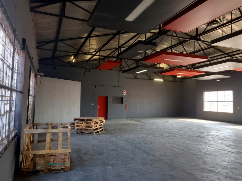 Spacious industrial utility space featuring exposed steel roof trusses, suspended acoustic ceiling panels, concrete flooring, and security window grilles.
