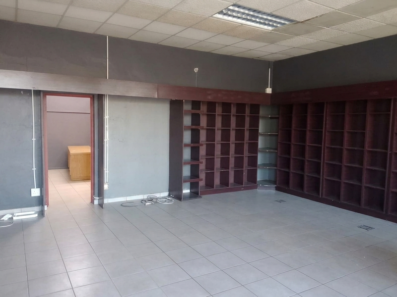 Empty commercial office space featuring extensive built-in shelving, tiled flooring, and a suspended ceiling with integrated lighting.