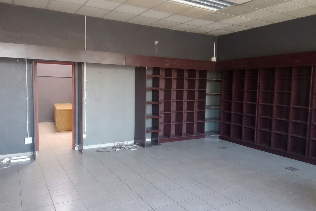 Empty commercial office space featuring extensive built-in shelving, tiled flooring, and a suspended ceiling with integrated lighting.