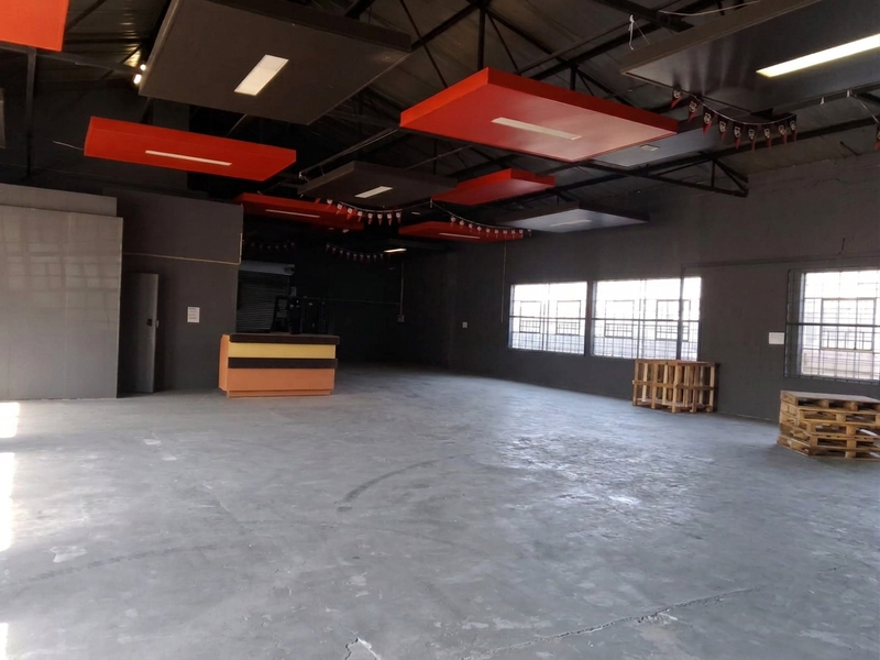 Spacious open-plan commercial unit featuring industrial concrete flooring, exposed ceiling trusses, suspended acoustic panels, and large steel-framed windows providing ample natural light.