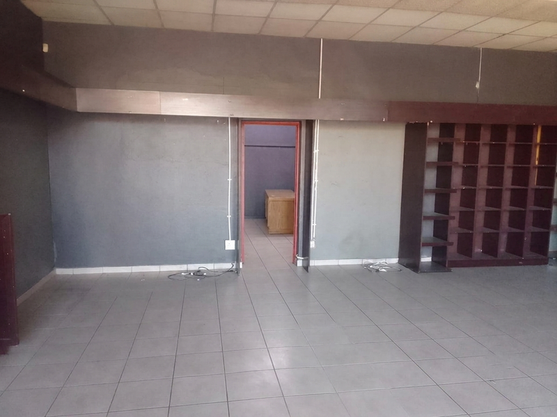 An empty commercial office space featuring tiled flooring, built-in shelving, and a suspended ceiling, ready for customization or fit-out.