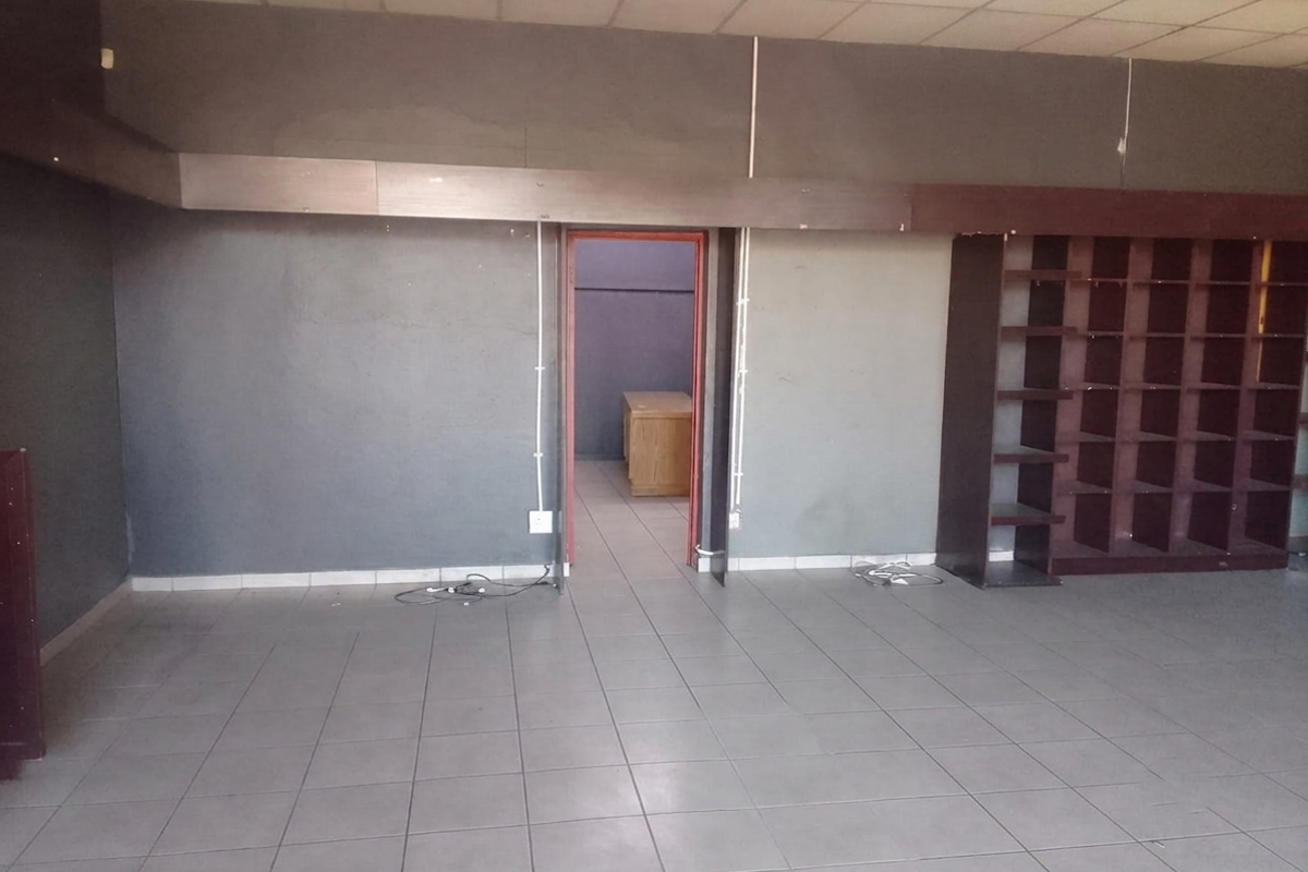 An empty commercial office space featuring tiled flooring, built-in shelving, and a suspended ceiling, ready for customization or fit-out.