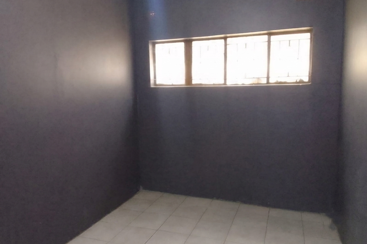 An empty bedroom featuring dark painted walls, tiled flooring, and a window fitted with security bars.