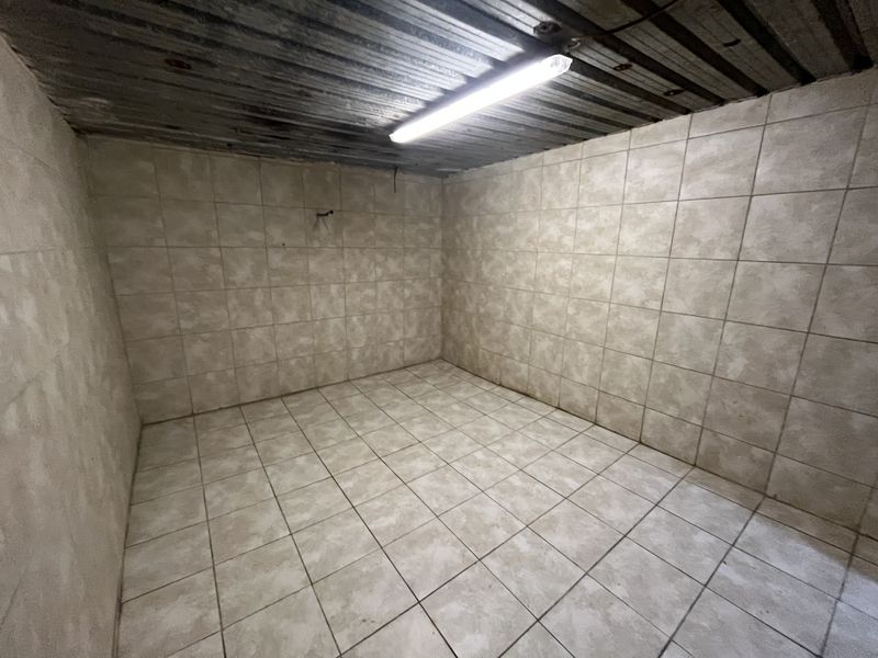 A vacant utility space featuring fully tiled walls and flooring with a corrugated metal ceiling and overhead fluorescent lighting.