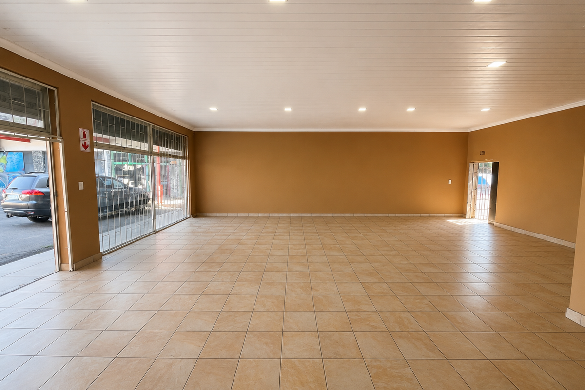A spacious, empty retail unit featuring neutral walls, tiled flooring, recessed ceiling lighting, and a large glass storefront with security gate access.