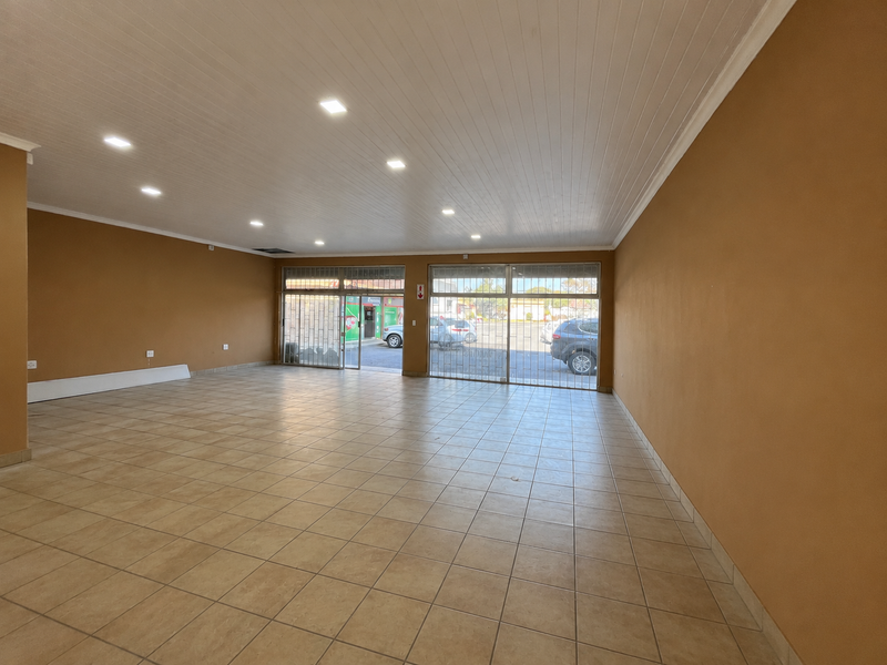 Spacious open-plan retail unit featuring tiled flooring, recessed downlighting, and secure glass storefront access, suitable for various commercial business applications.