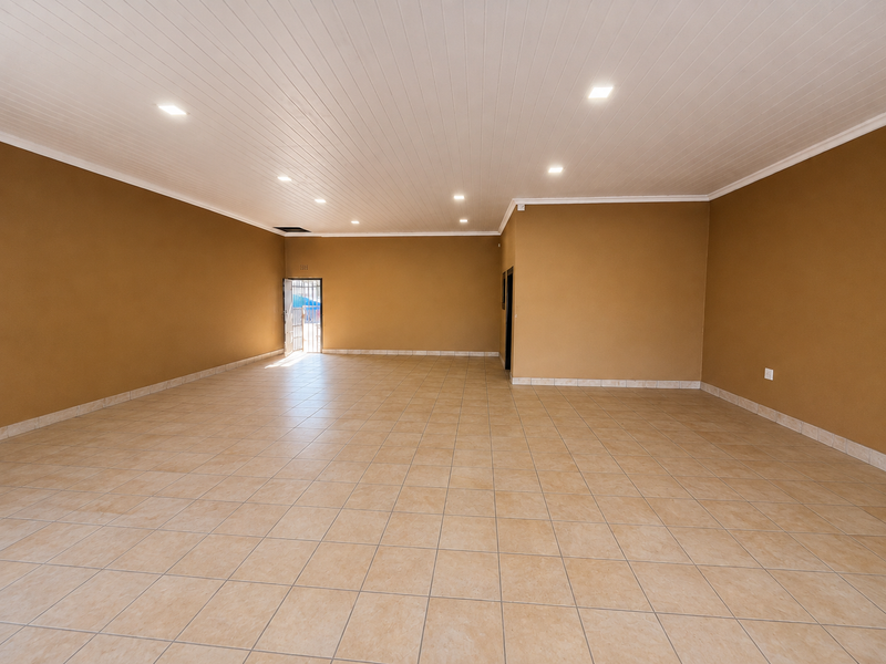 A spacious, empty open-plan retail area featuring neutral tiled flooring, a clean panelled ceiling with recessed lighting, and a secure entrance.