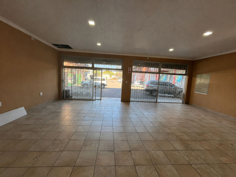 Spacious open-plan retail unit featuring large glass storefront windows with security gates, tiled flooring, and recessed ceiling lighting, suitable for various commercial business applications.