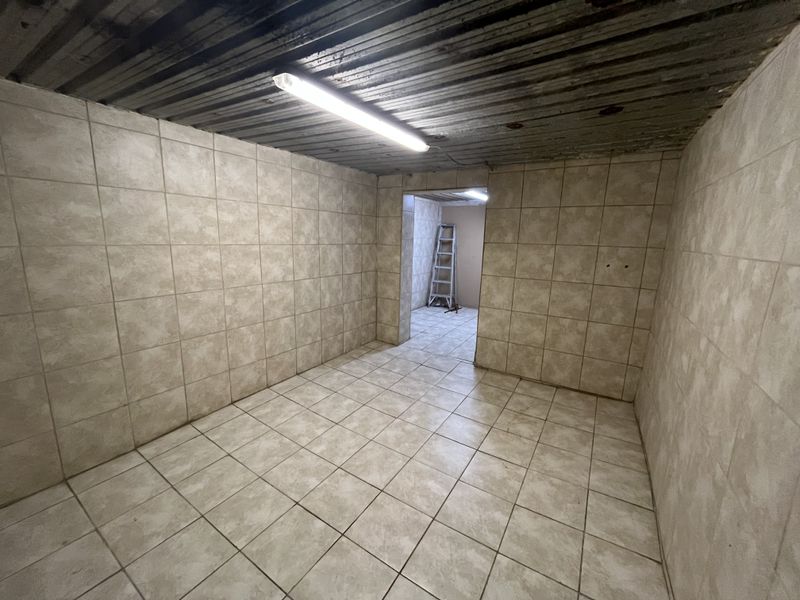 A vacant utility space featuring fully tiled walls and flooring with a corrugated metal ceiling and functional strip lighting.