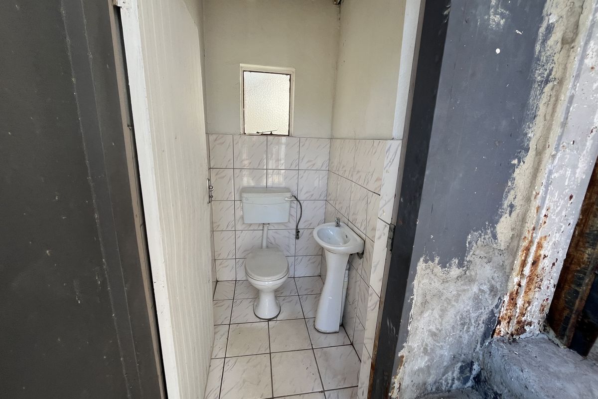 A small, basic bathroom featuring a toilet and pedestal basin with tiled finishes, currently showing significant signs of wear and surface deterioration.