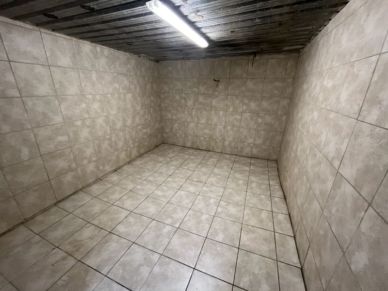 A vacant utility space featuring fully tiled walls and flooring with a corrugated metal ceiling and overhead fluorescent lighting.
