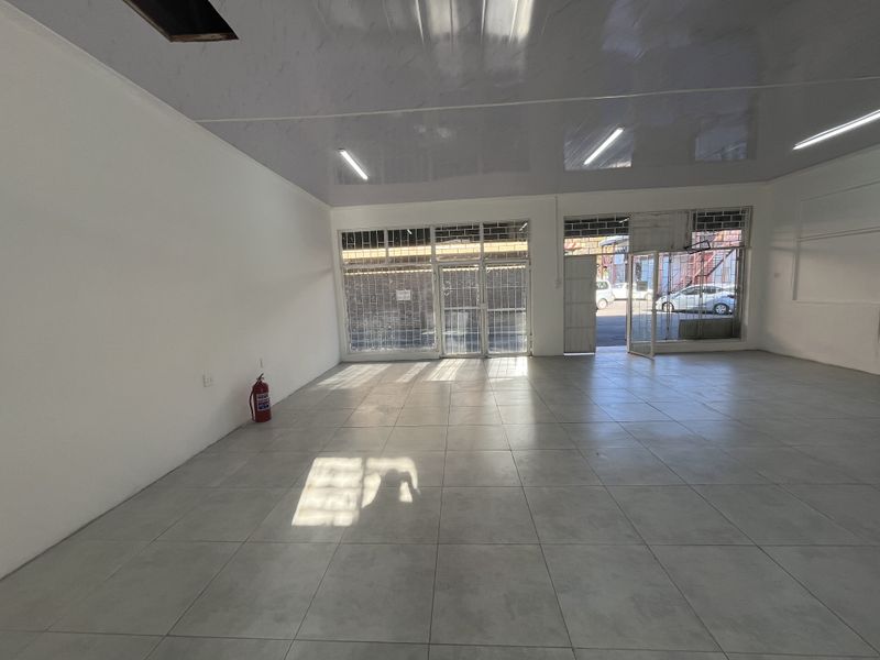 Spacious open-plan retail unit featuring tiled flooring, a suspended ceiling with integrated lighting, and secure glass storefront access.