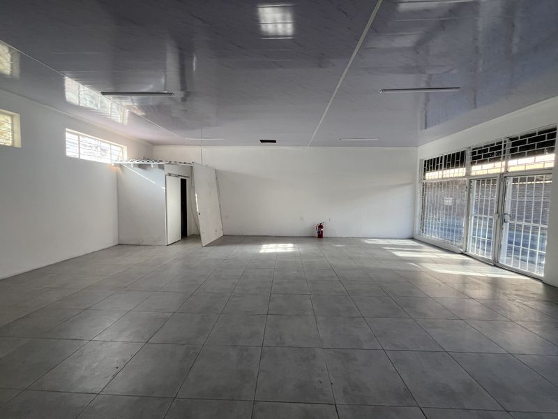 An open-plan retail space featuring tiled flooring, a suspended ceiling, and secure glass frontage with security gates.