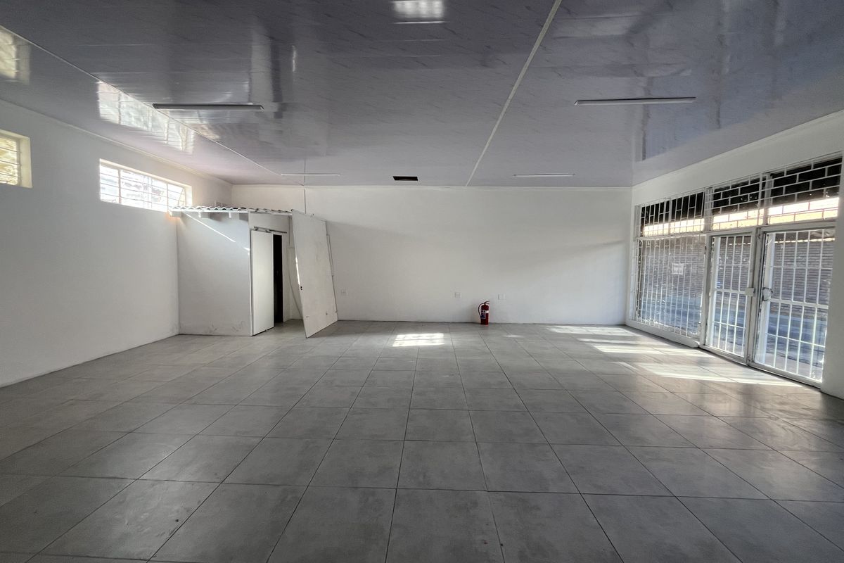 An open-plan retail space featuring tiled flooring, a suspended ceiling, and secure glass frontage with security gates.