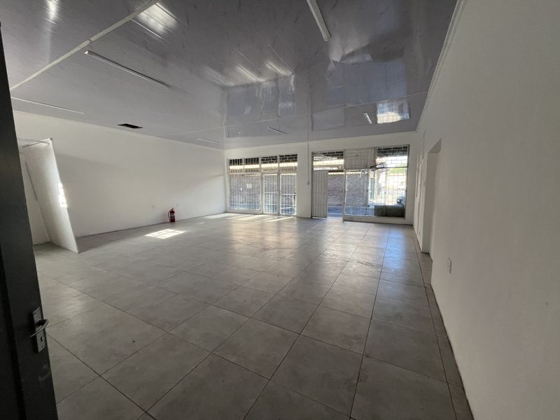 Spacious open-plan retail unit featuring large display windows, security gates, tiled flooring, and a suspended ceiling, suitable for various commercial business applications.