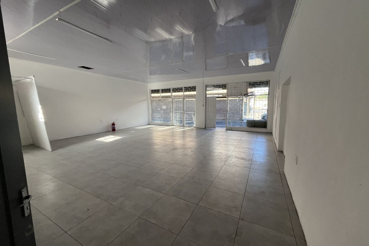 Spacious open-plan retail unit featuring large display windows, security gates, tiled flooring, and a suspended ceiling, suitable for various commercial business applications.