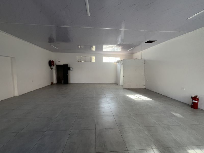 A spacious, empty retail unit featuring modern grey tiled flooring, a clean suspended ceiling, and an integrated cold storage unit.