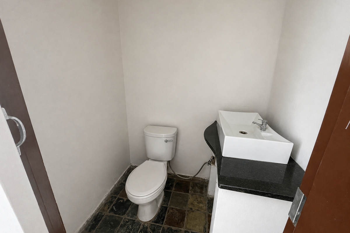 A compact powder room featuring a white toilet, a modern vessel sink set on a black granite vanity countertop, and dark stone tile flooring.
