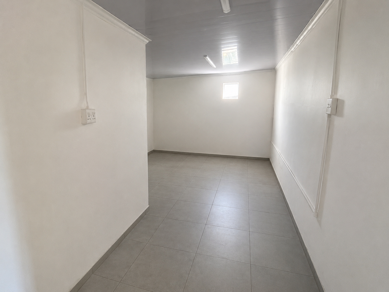 A clean, empty utility space featuring neutral tiled flooring, white walls, and surface-mounted electrical fixtures, suitable for various commercial or storage purposes.