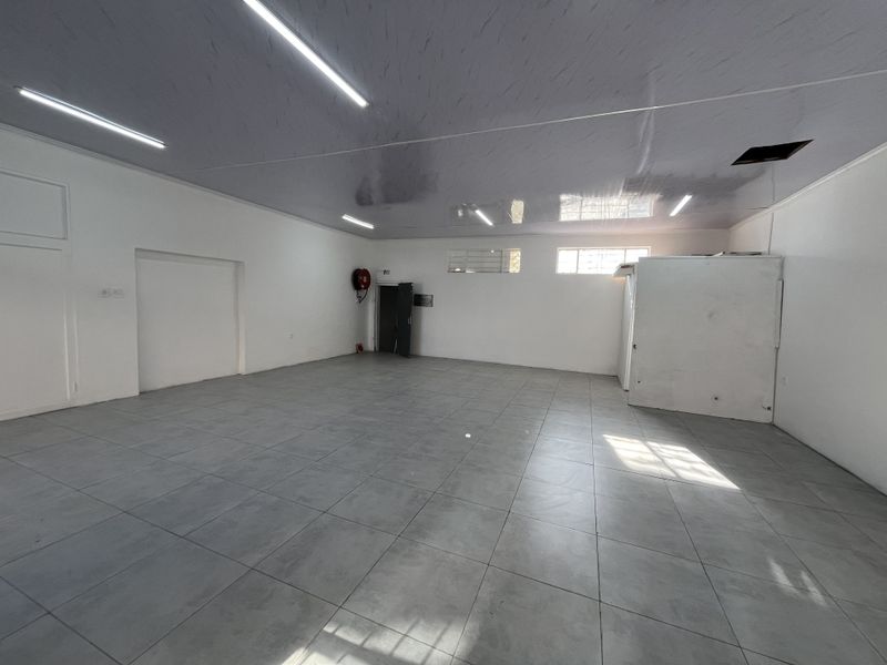 A spacious, empty retail open-plan area featuring tiled flooring, fluorescent lighting, and a built-in storage unit, suitable for various commercial business applications.