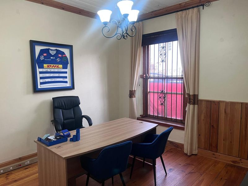 A functional office space featuring timber flooring, wainscoting, and a window fitted with security bars, providing a professional work environment.